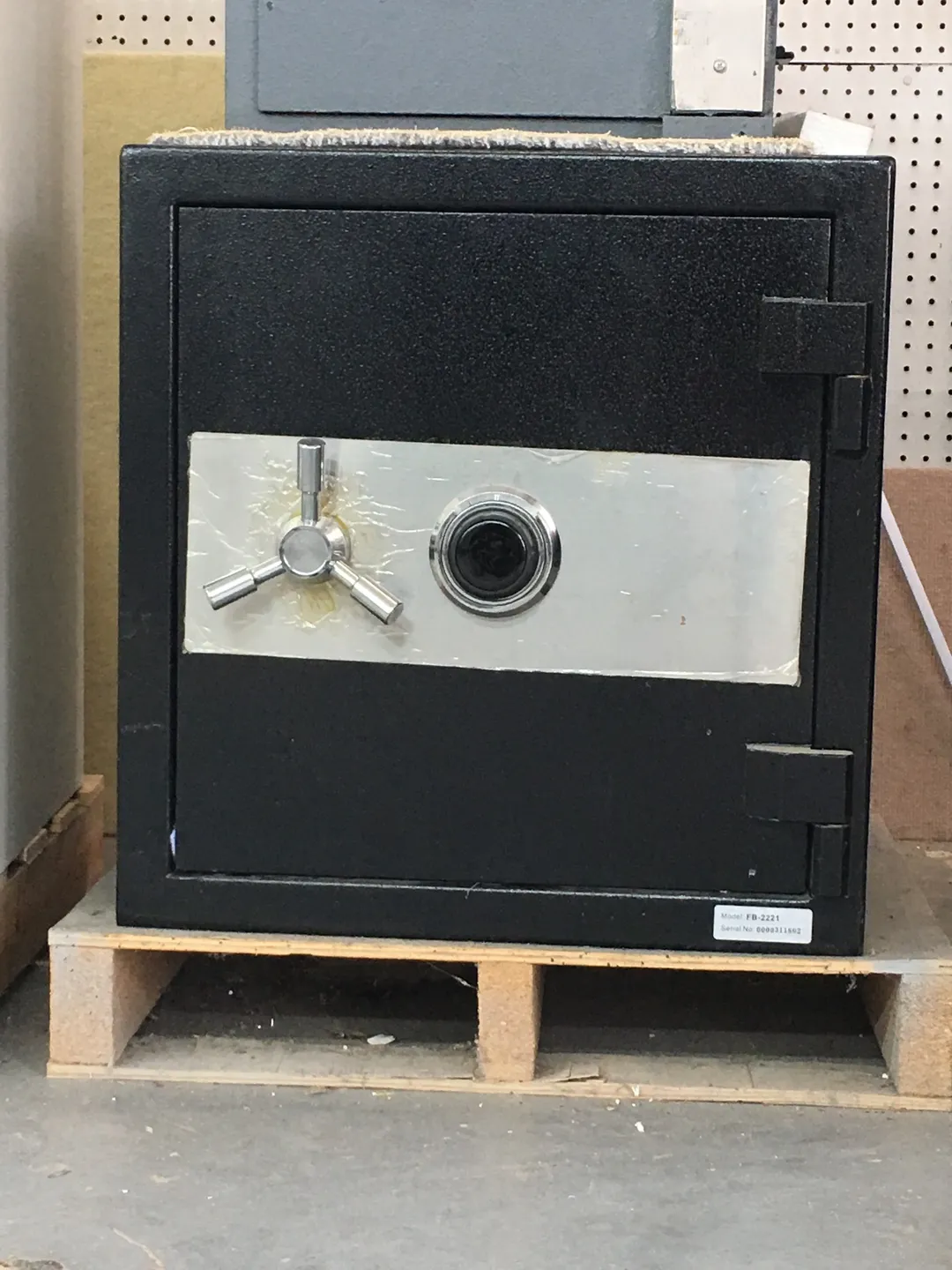 A black safe with a combination dial and handle on a wooden pallet.